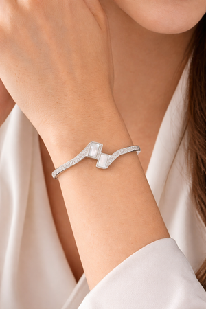 Office wear jewellery styling showing silver geometric stone bangle on woman's wrist paired with white formal shirt.