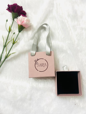 Pink jewelry box with 'Sarya' branding on a white background with flowers.